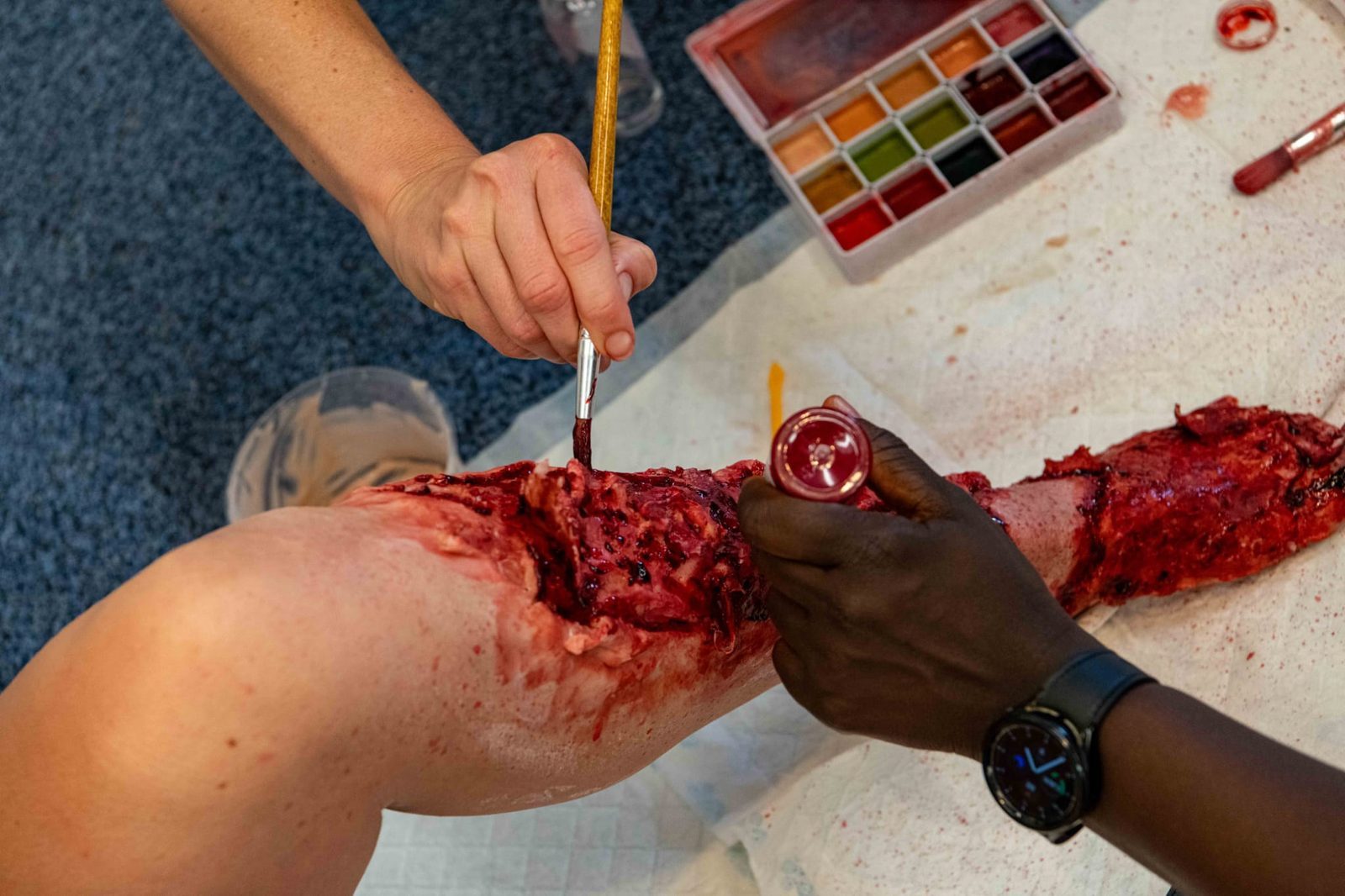 Two people working colour into an open leg wound with a brush and palette during a training session