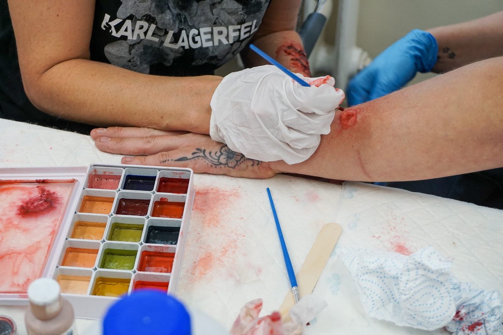 A gloved delegate working a forearm wound with a brush, colour palette and materials laid out alongside