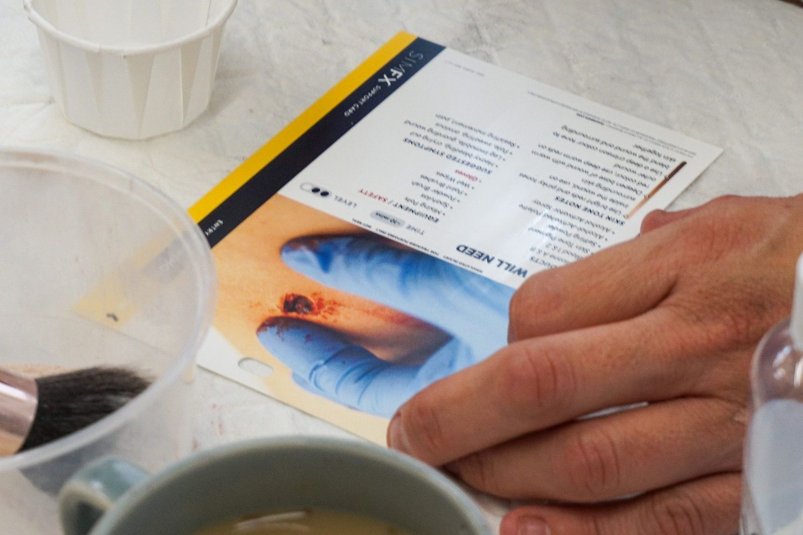 Hands holding a SIMFX Support Card at the bench, materials and a mixing pot in frame