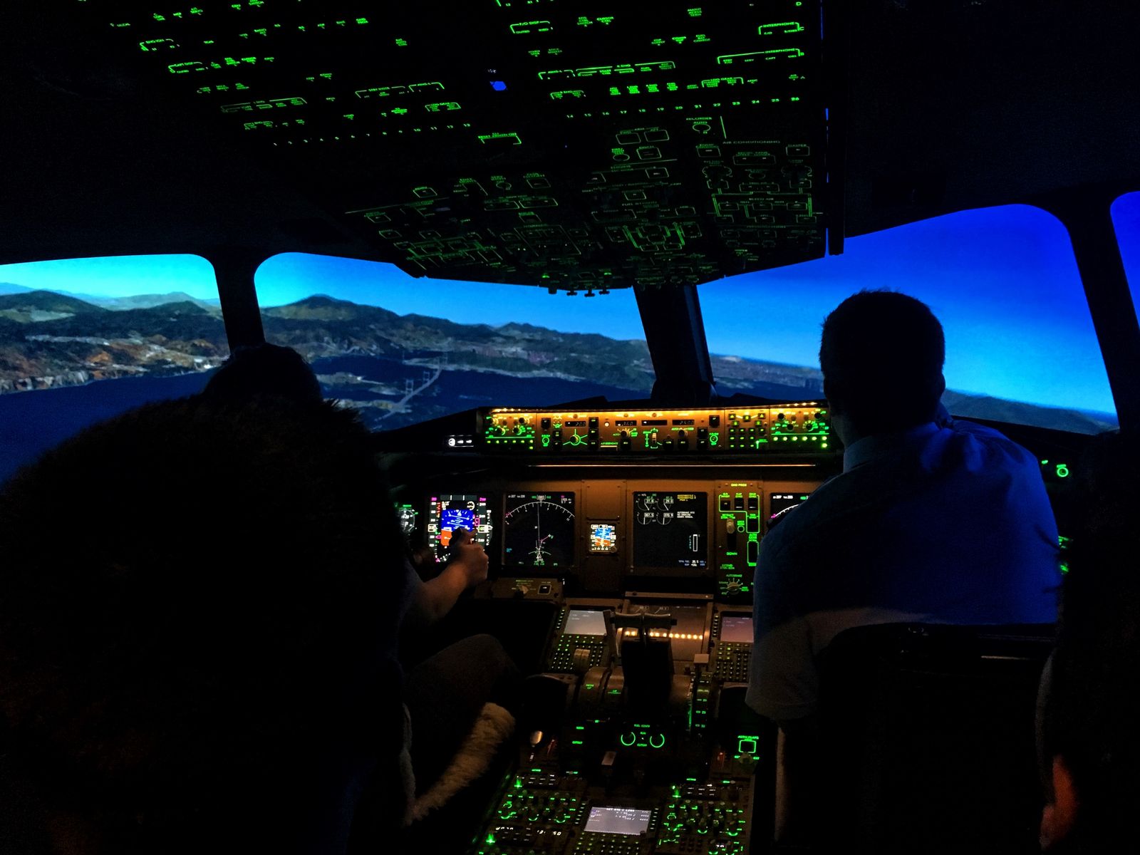 Two crew at the controls of a full-flight simulator flight deck at night