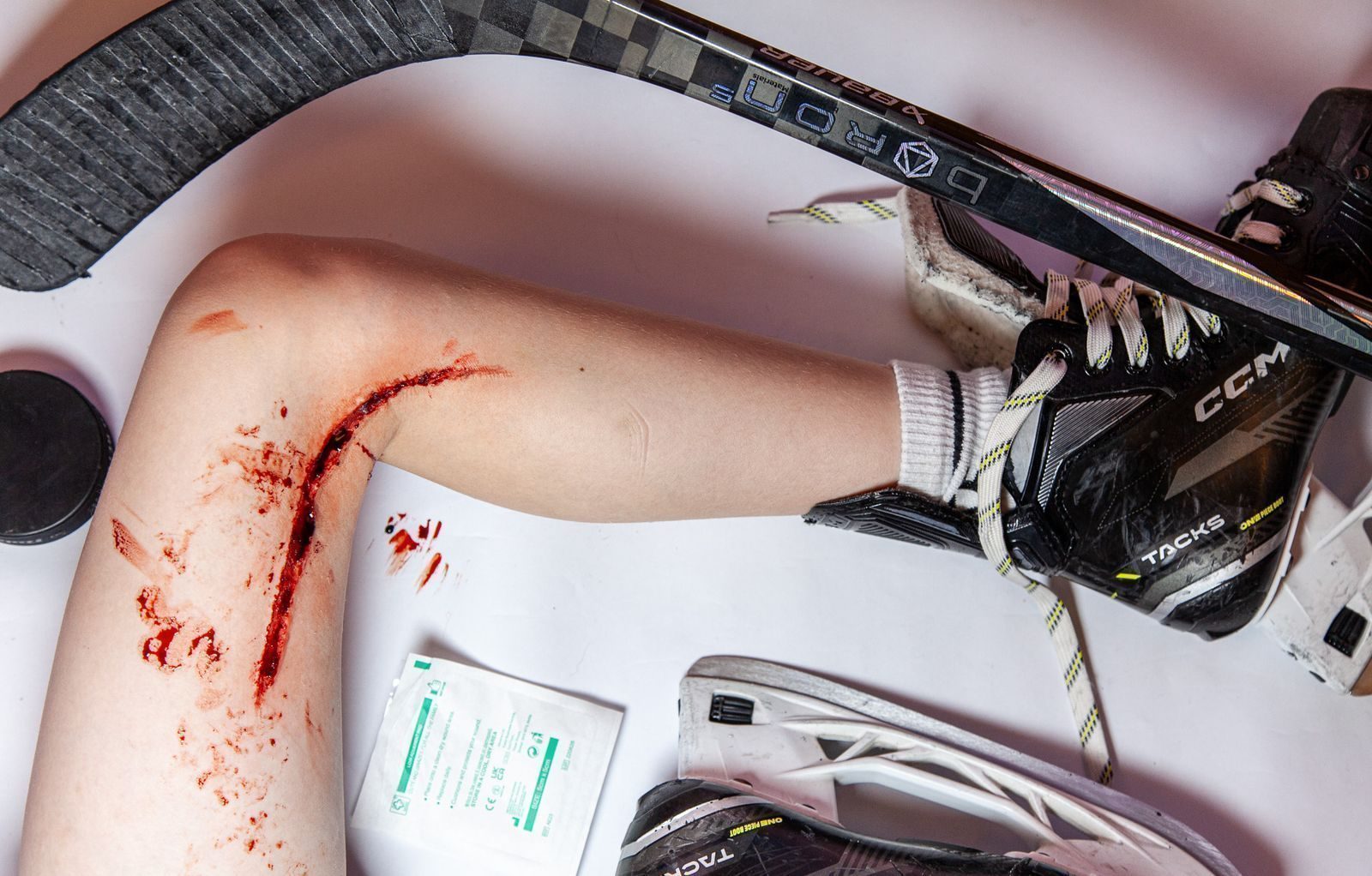 Simulated leg laceration for an ice hockey scenario, shown with stick, skates and a wound dressing